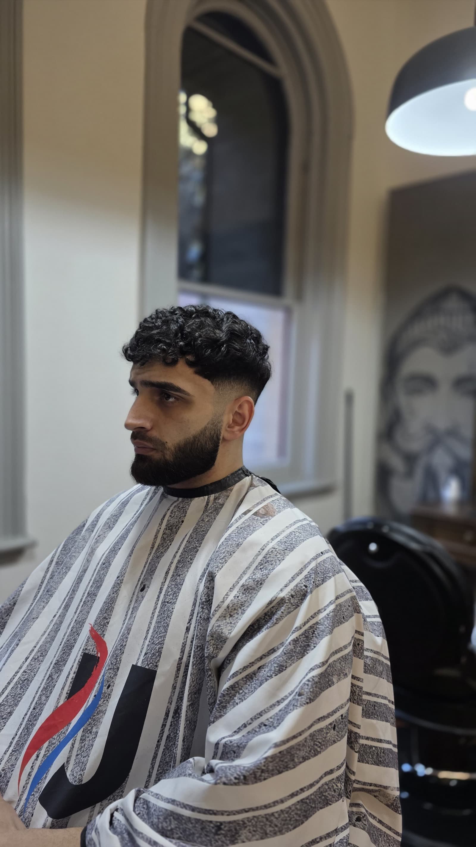 A client with short faded sides and a trimmed beard in an UPTOWN Barbers chair